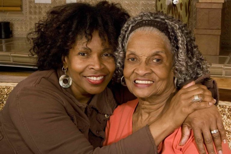 A senior woman and her adult daughter smile for a picture.