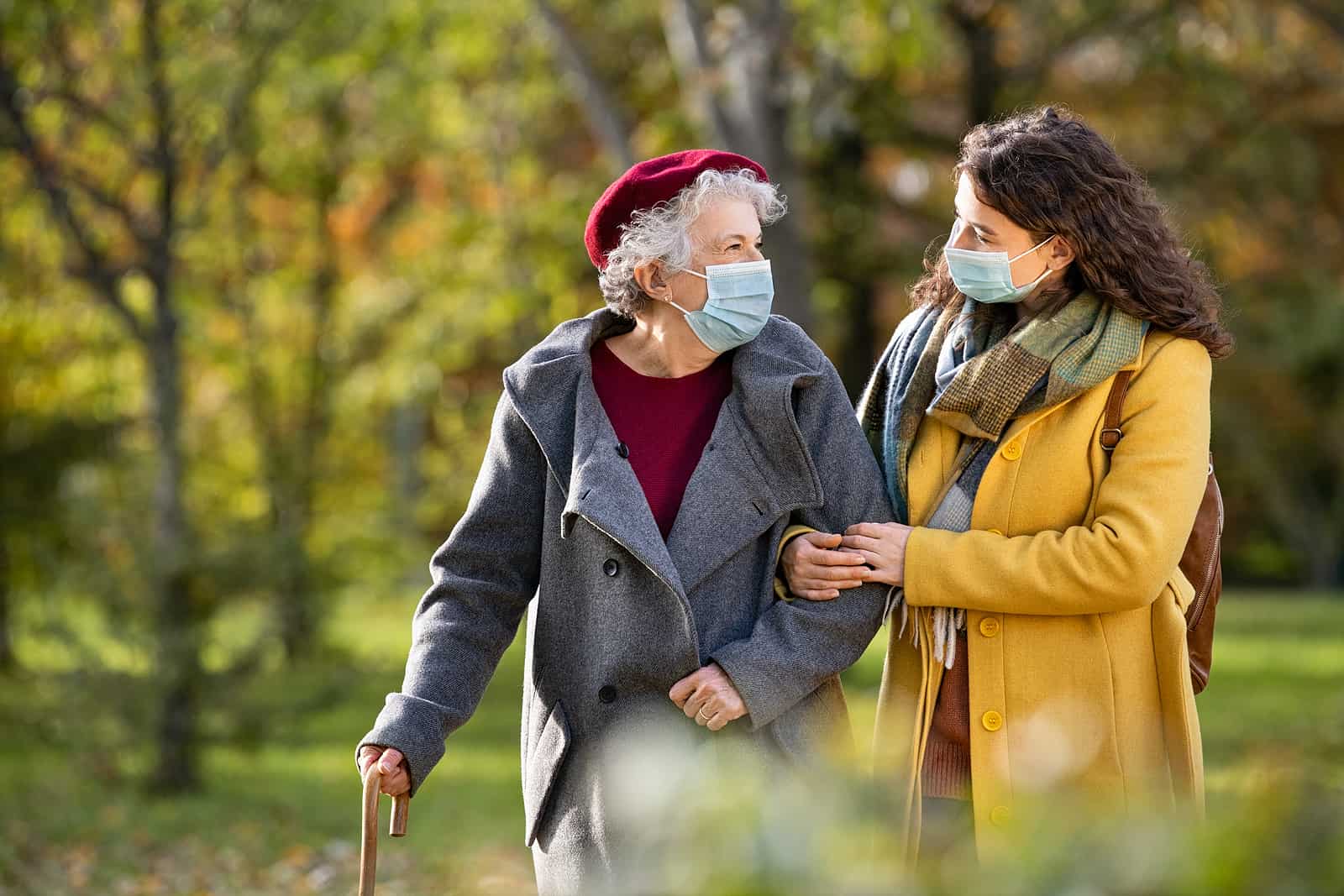 A senior woman and her daughter walk outdoors wearing masks.