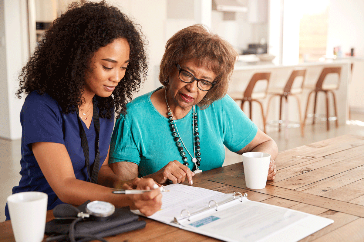A senior woman and a healthcare worker fill out paperwork together.